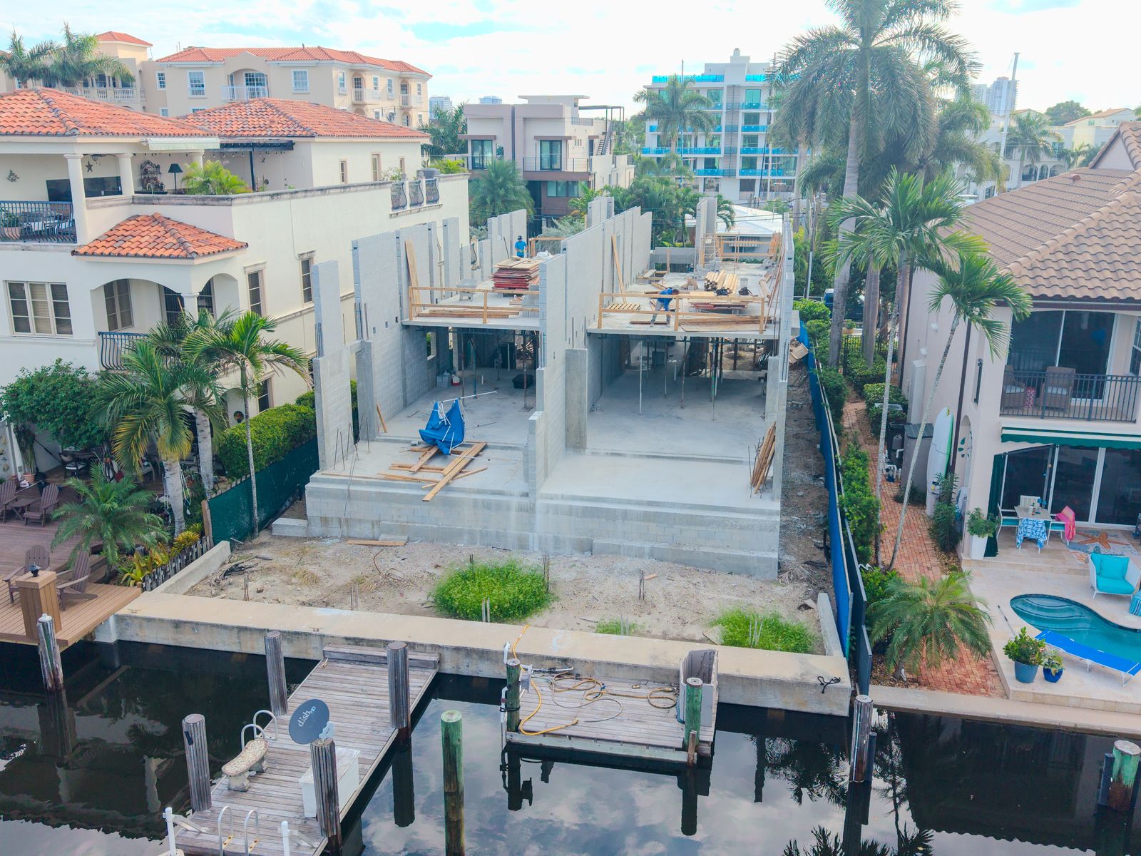 Aerial view of a canal-front spec home under construction between finished homes with docks